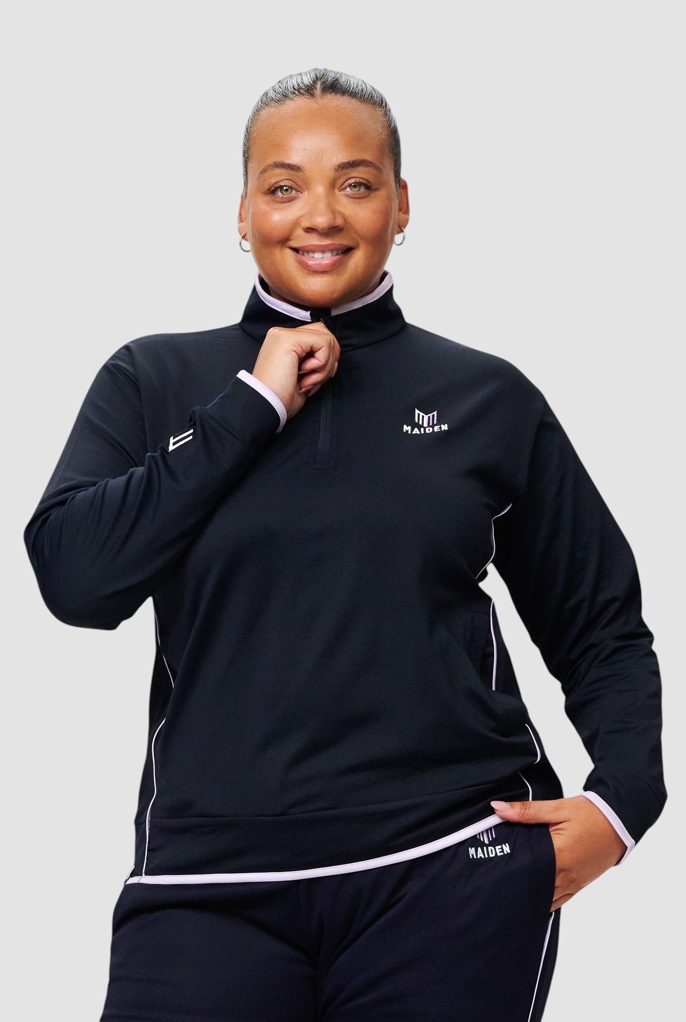 Woman wearing a black Maiden Cricket Century Zipper midlayer with light pink trim and quarter-zip detail.