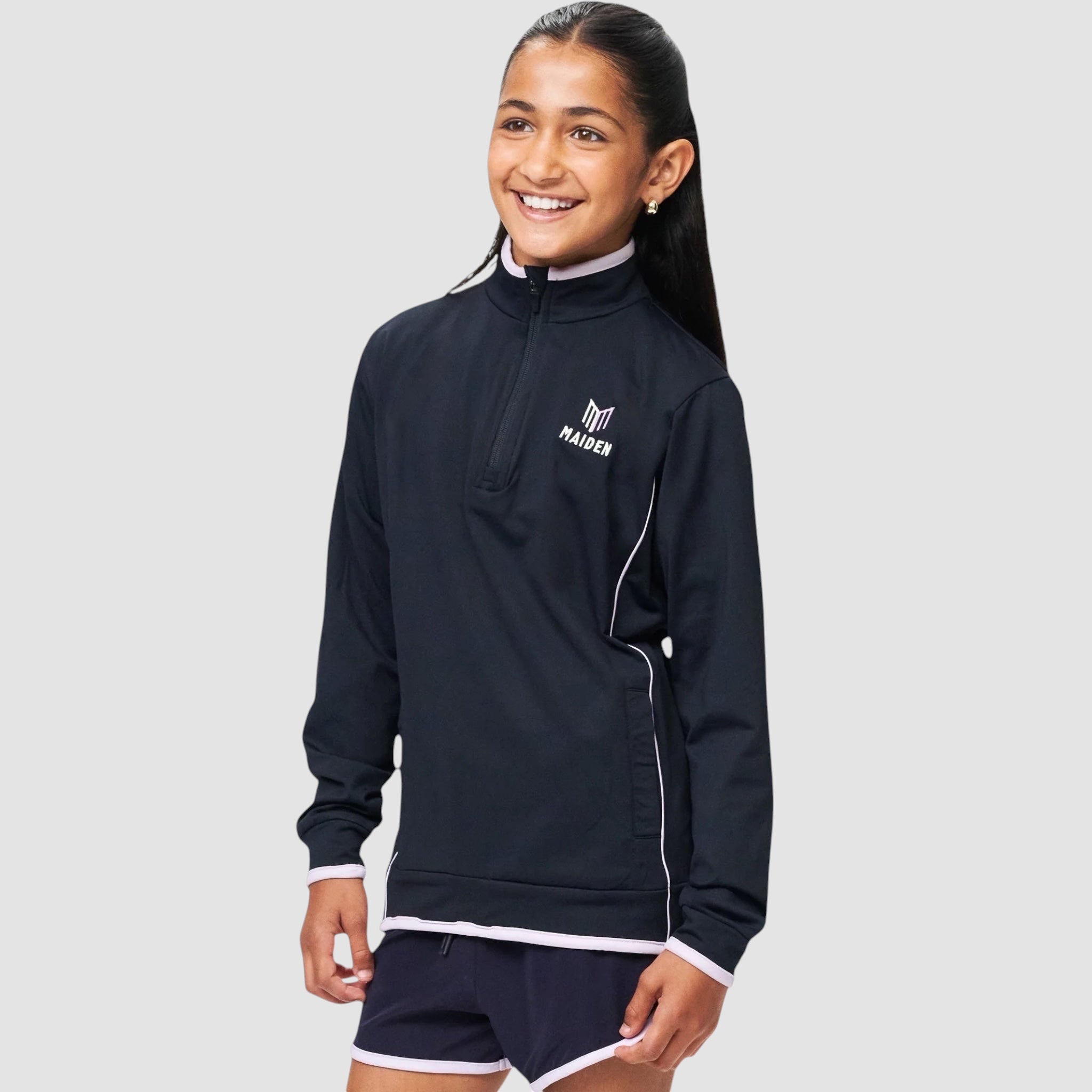 Young girl wearing a navy Maiden Cricket quarter-zip midlayer with light pink trim and logo, designed for sports.