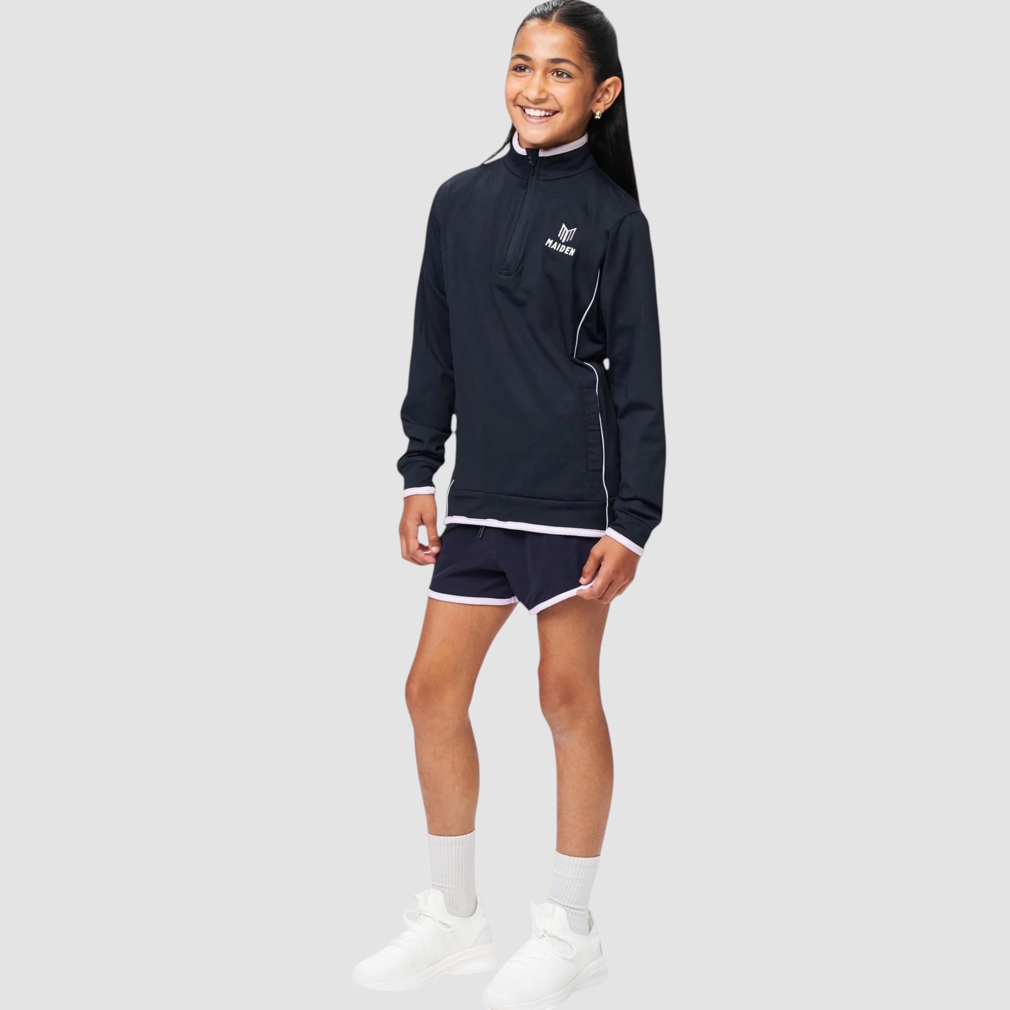 Young girl wearing a Maiden Cricket navy blue 1/4 zip midlayer with white trim and matching athletic shorts
