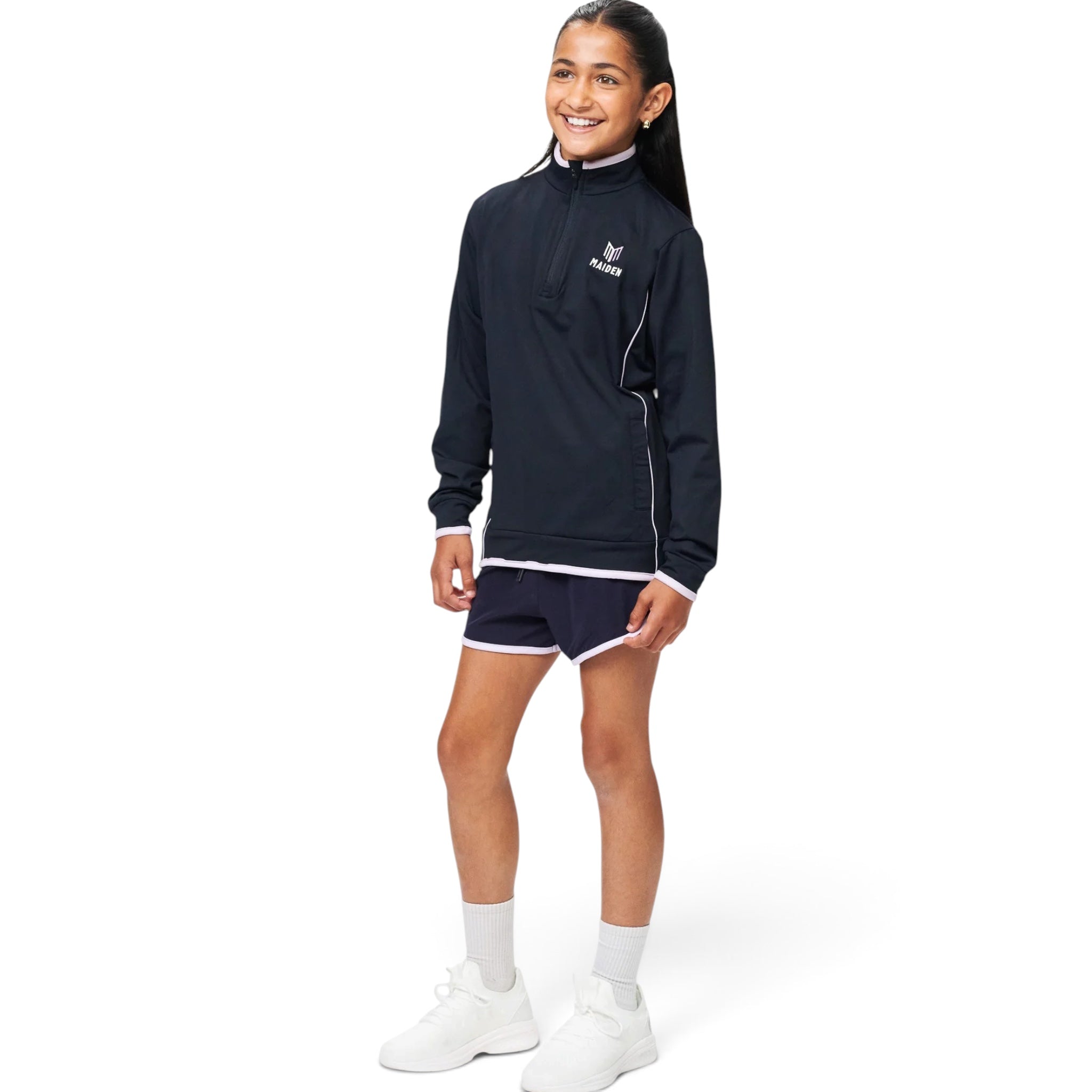 A girl wearing a Maiden Cricket navy blue quarter-zip midlayer with white trim and matching athletic shorts.