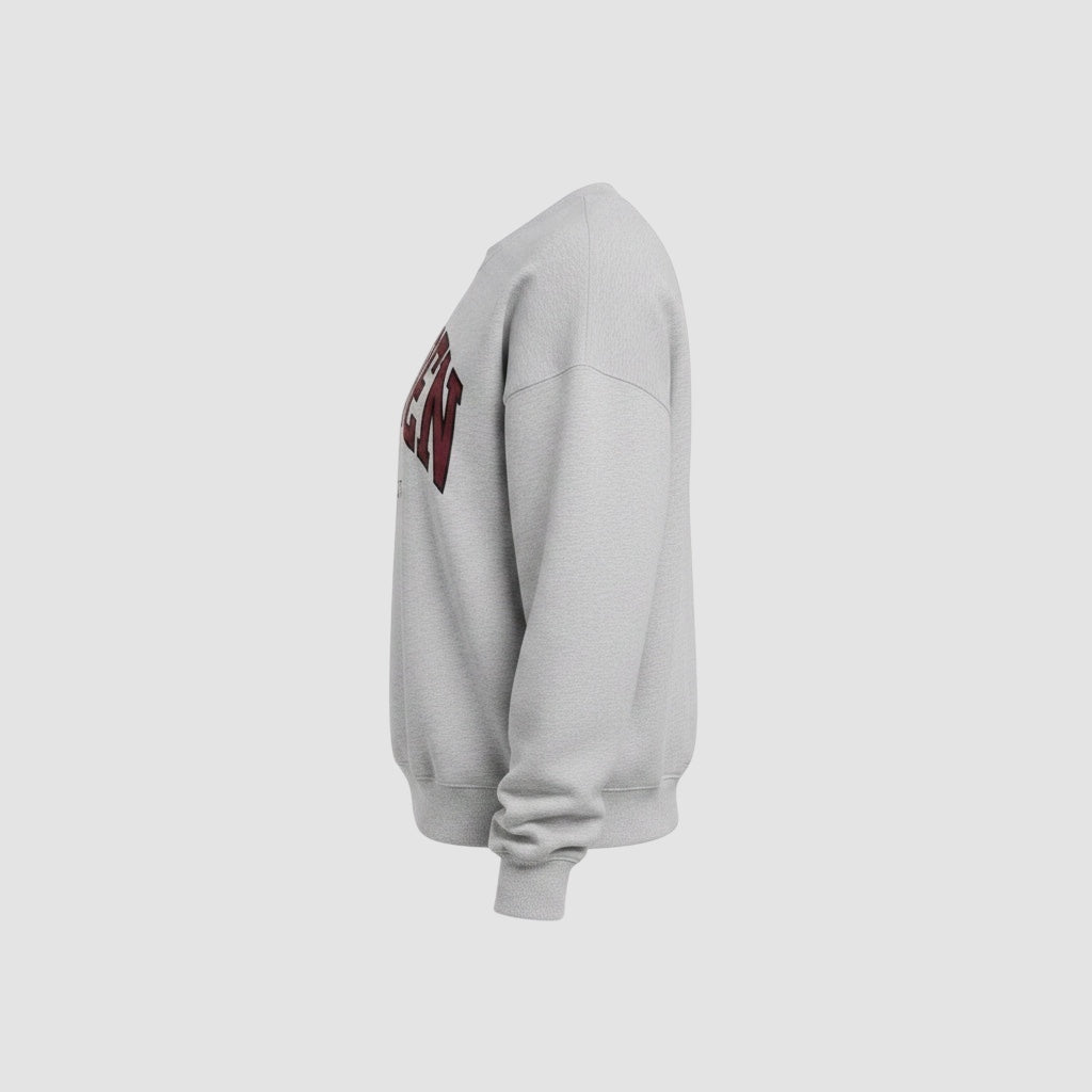 Side view of a Maiden Cricket heather grey crewneck sweatshirt with a maroon and black collegiate graphic.