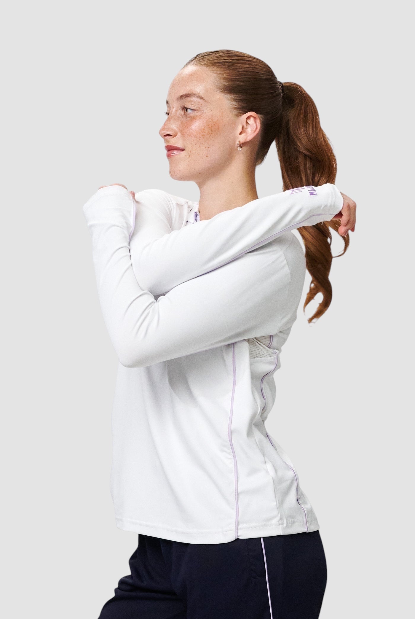 Maiden Cricket white long-sleeve performance top with purple trim and mesh underarm panels worn by a female athlete