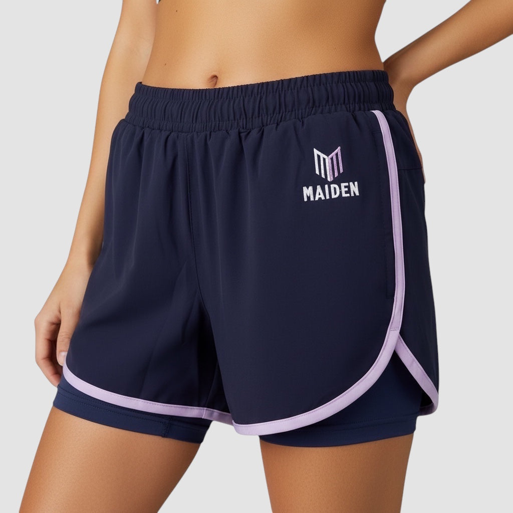 Maiden Cricket navy blue athletic shorts with built-in undershorts, lavender trim, and logo on a female model.