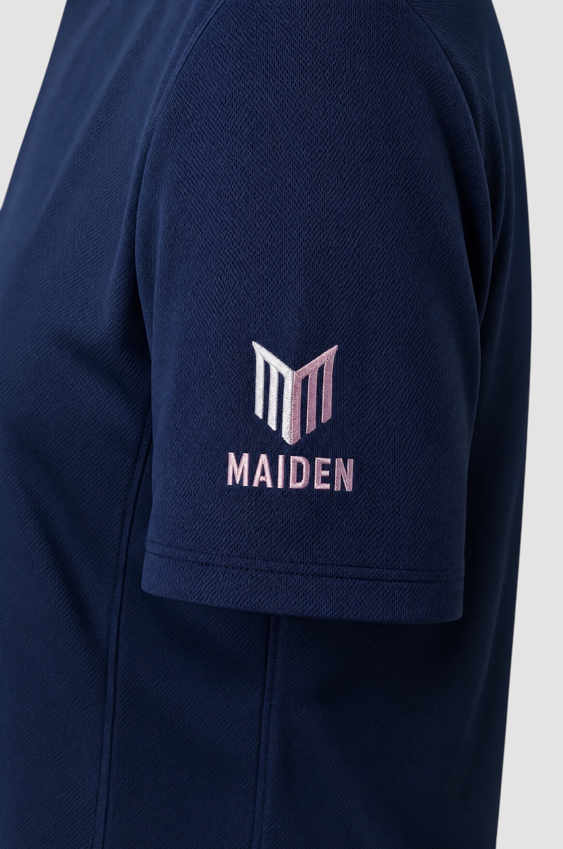 Close-up of the navy blue Maiden Cricket Women's World Cup t-shirt sleeve featuring a pink and white logo embroidery.
