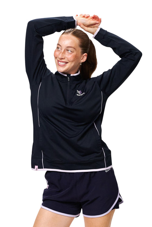 Maiden Cricket women's navy quarter-zip midlayer with light pink trim, worn by a smiling athlete with arms raised.