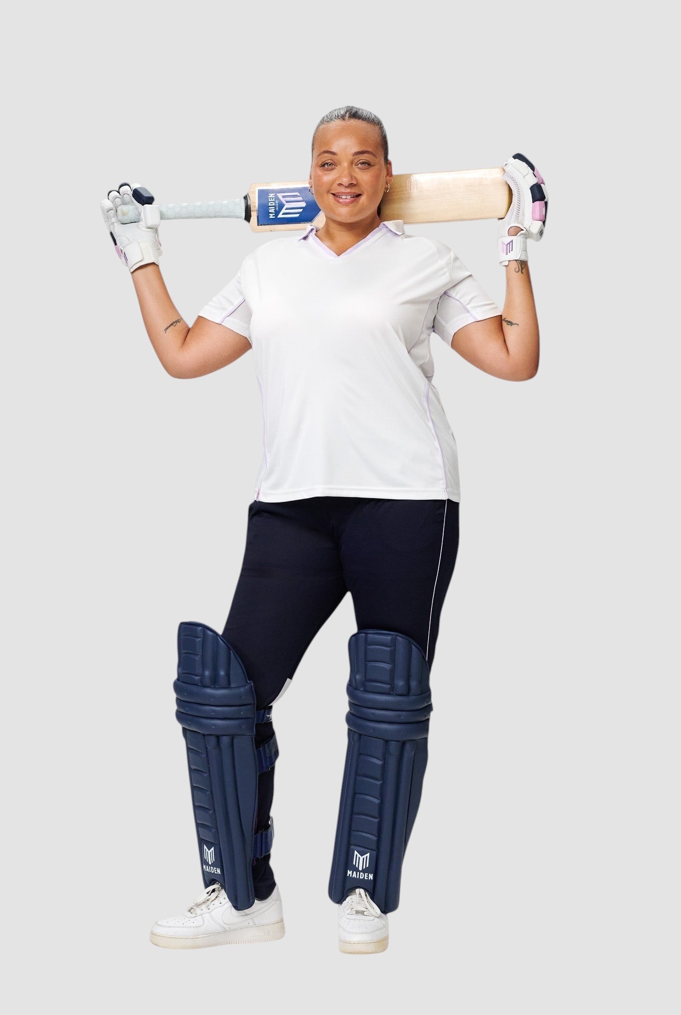 Female cricketer wearing Maiden Cricket navy batting pads designed for a secure, ergonomic fit with a cricket bat