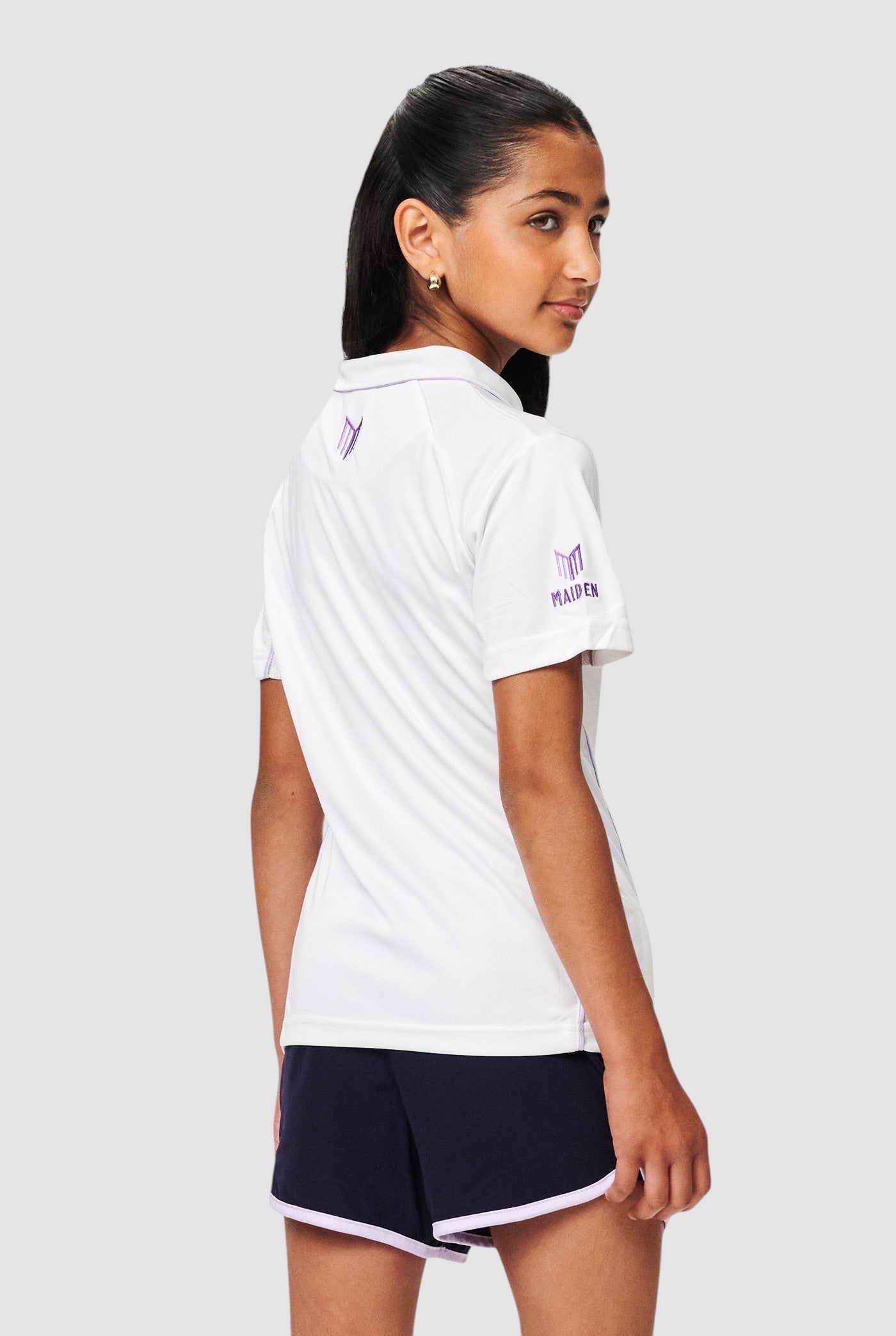 Maiden Cricket white performance polo shirt with purple piping and branding, worn by a girl from the back view.