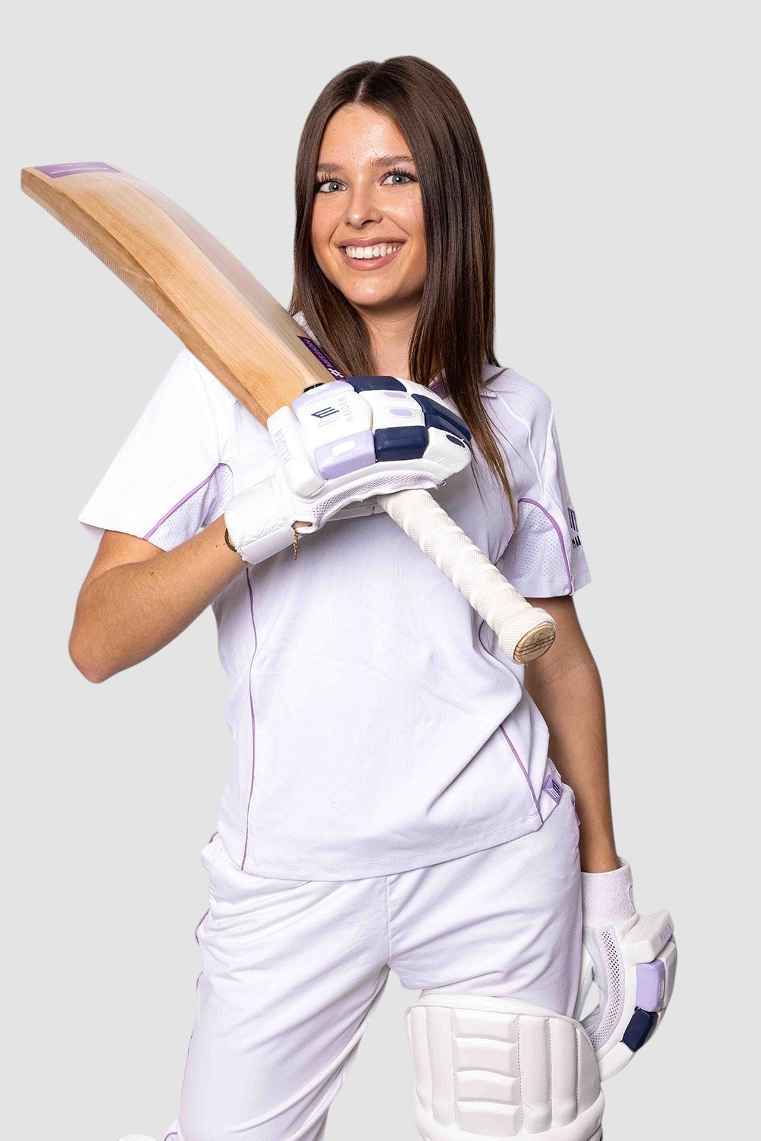 A female cricketer wearing a white Maiden Cricket performance polo with purple piping, holding a wooden cricket bat.