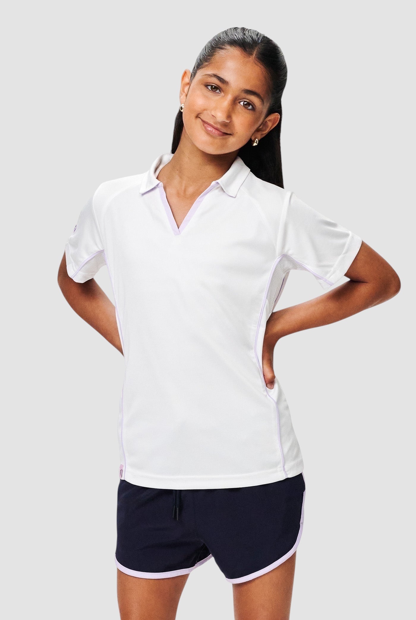Young girl wearing a white Maiden Cricket performance polo shirt with purple piping and breathable mesh panels.