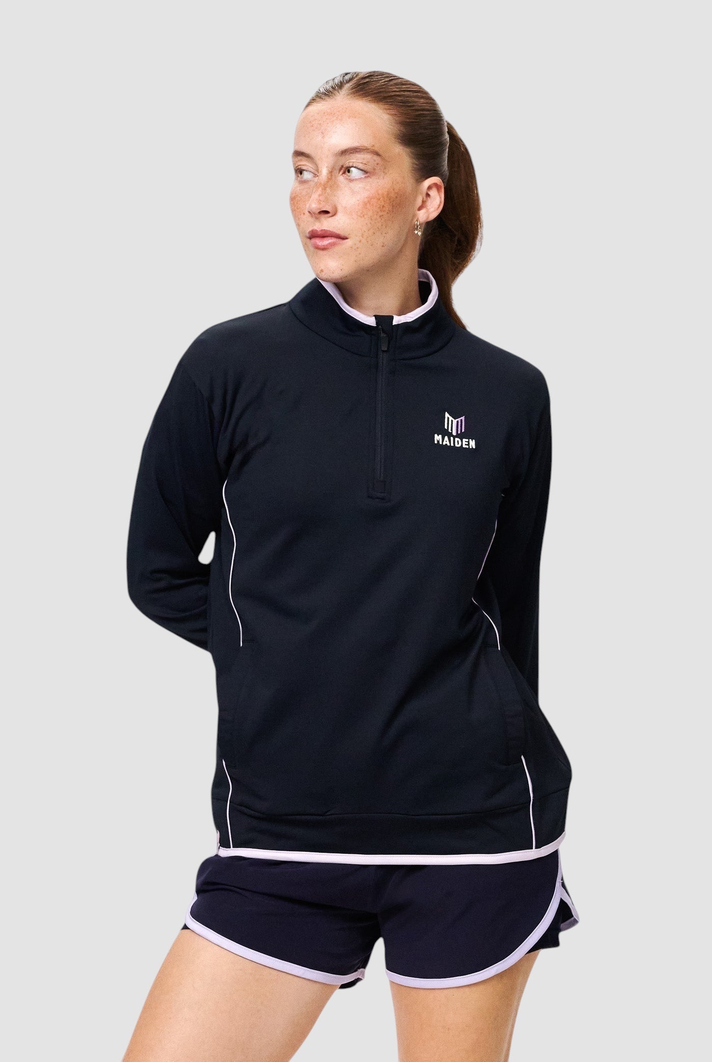 Maiden Cricket women's black quarter-zip midlayer with white trim, worn by a model with hands behind her back.