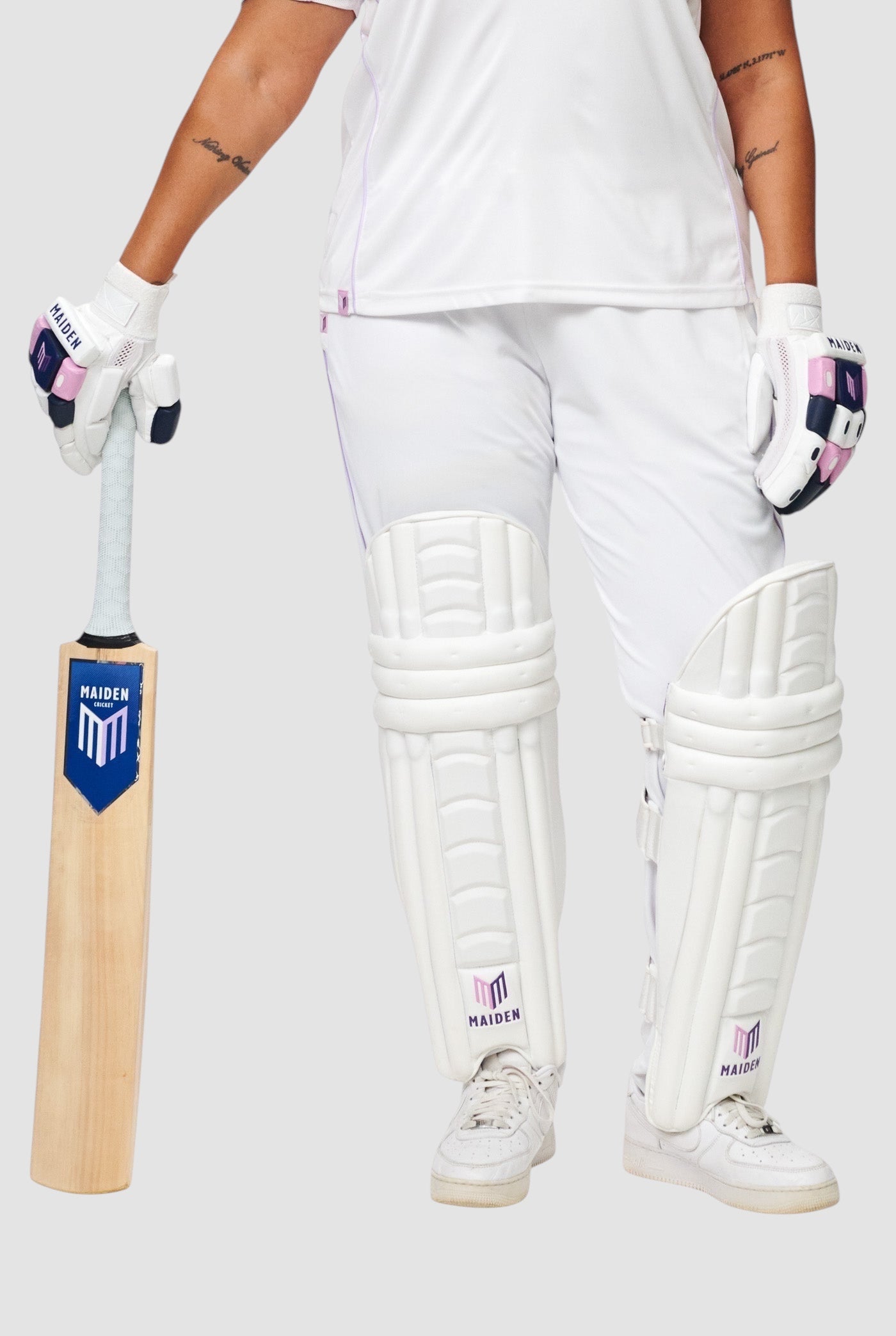 Maiden Cricket women's white batting pads with ergonomic design, worn by a player holding a cricket bat and gloves.