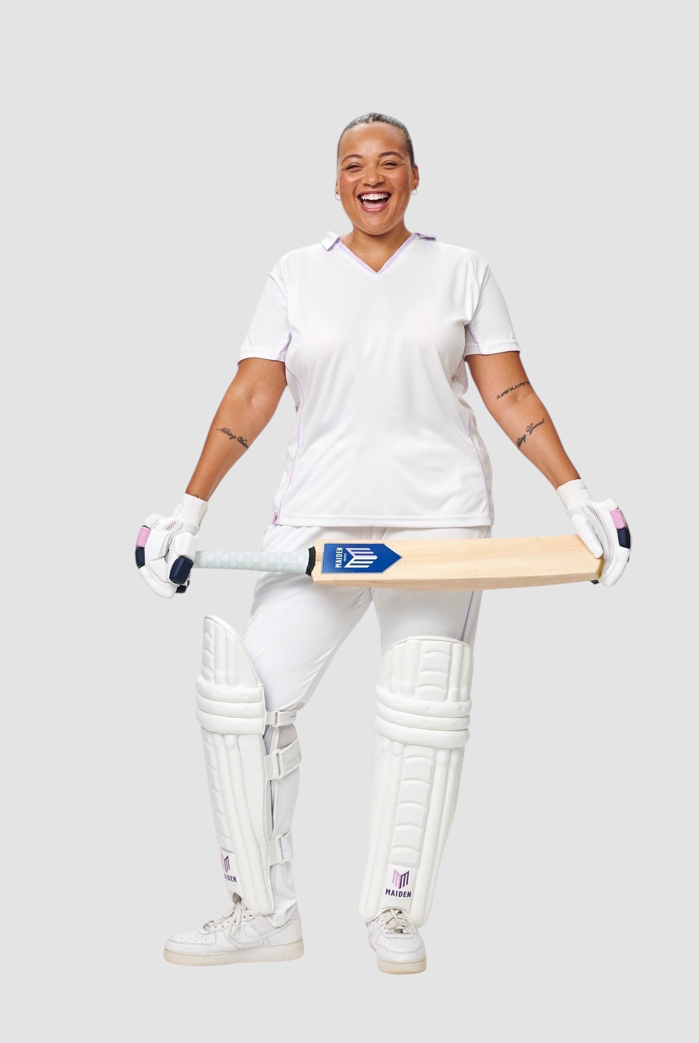 Maiden Cricket women's white batting pads with ergonomic knee curve, worn by a smiling female cricketer in white kit.
