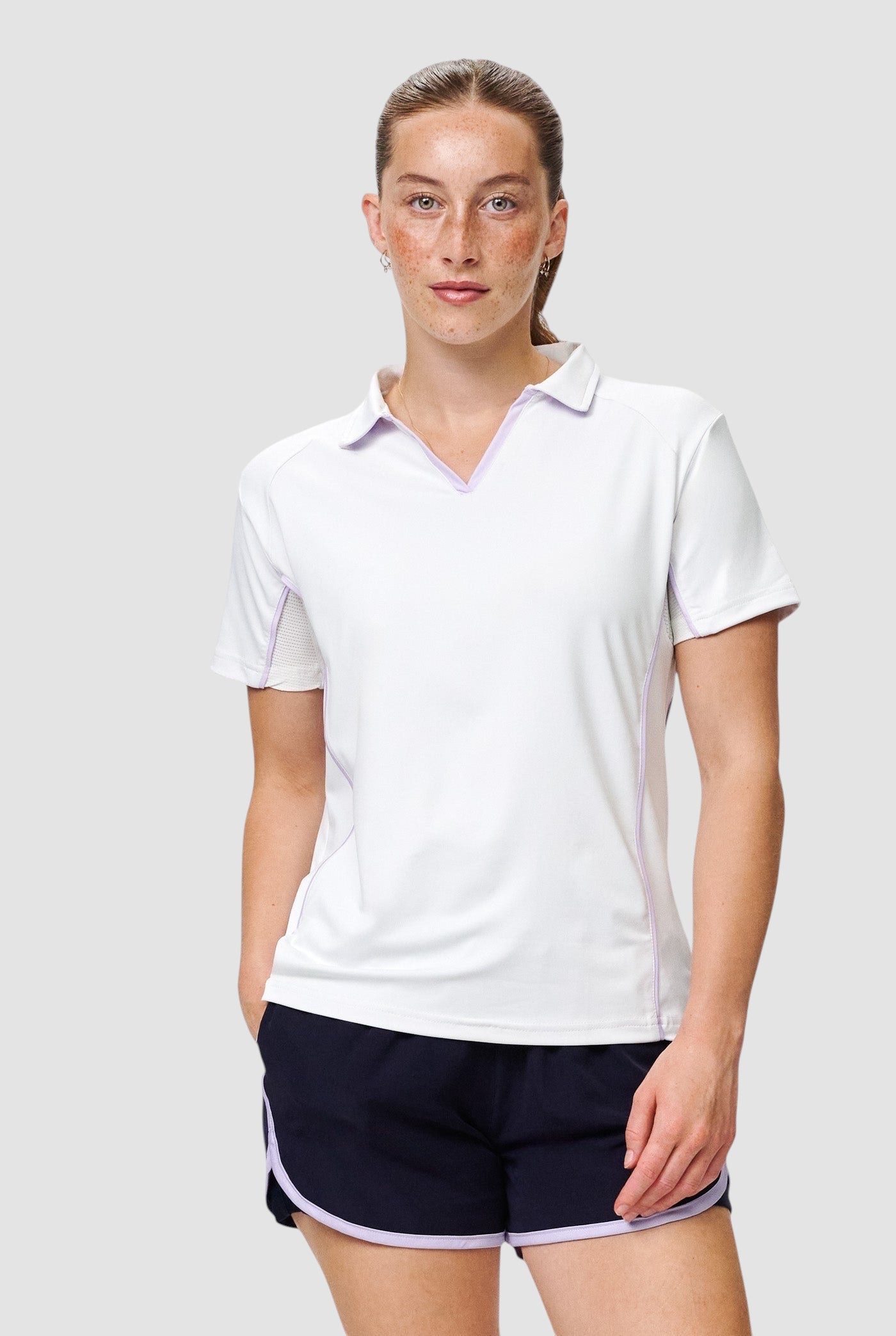 Female athlete wearing a white Maiden Cricket Mid-On Top with a V-neck, mesh underarm panels, and light purple trim.